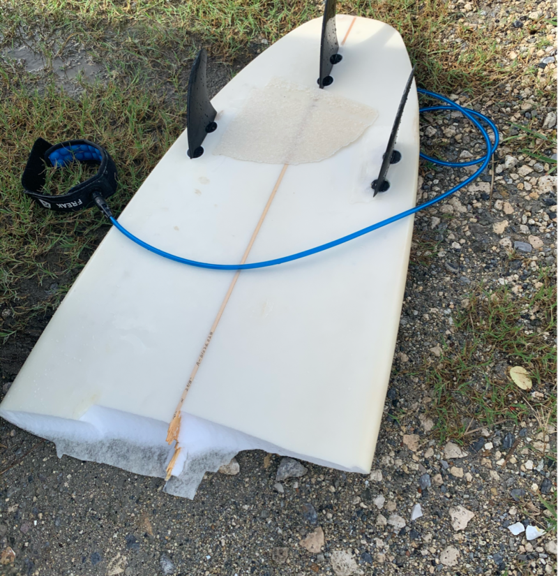 A white surfboard snapped in half, lying on the ground